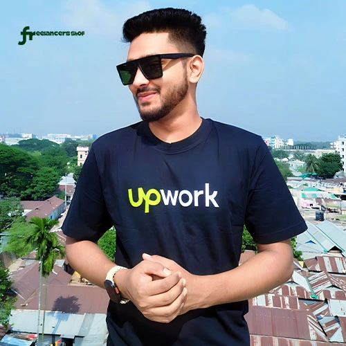 কালো আপওয়ার্ক লোগো প্রিন্ট করা টি-শার্ট পরা ব্যক্তি বাইরে দাঁড়িয়ে আছেন।